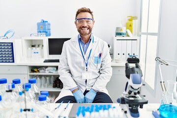 Wall Mural - Middle age man working at scientist laboratory looking positive and happy standing and smiling with a confident smile showing teeth