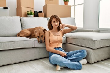 Sticker - Young caucasian girl wearing casual clothes sitting on the floor with dog at home with angry face, negative sign showing dislike with thumbs down, rejection concept