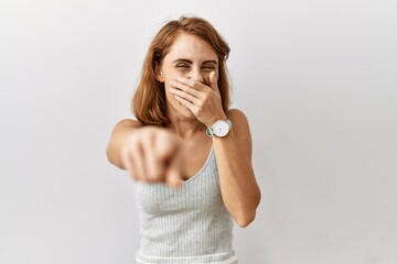 Sticker - Beautiful caucasian woman standing over isolated background laughing at you, pointing finger to the camera with hand over mouth, shame expression