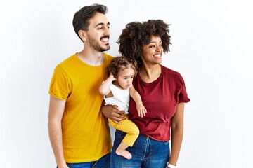 Interracial young family of black mother and hispanic father with daughter looking away to side with smile on face, natural expression. laughing confident.