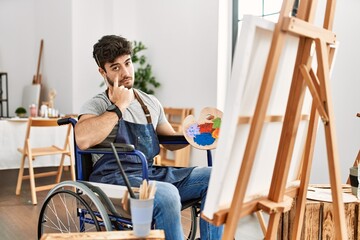 Sticker - Young hispanic man sitting on wheelchair painting at art studio pointing to the eye watching you gesture, suspicious expression