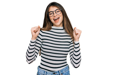 Sticker - Young beautiful teen girl wearing casual clothes and glasses celebrating surprised and amazed for success with arms raised and open eyes. winner concept.