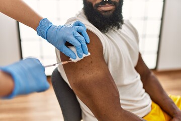 Hands of nurse woman injecting covid-19 vaccine to african amercian man at the clinic.