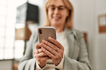 Wall Mural - Middle age businesswoman smiling happy using smartphone at the office.