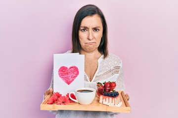 Poster - Middle age hispanic woman holding tray with breakfast food and heart draw depressed and worry for distress, crying angry and afraid. sad expression.