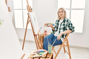 Sticker - Young artist woman painting on canvas at art studio smiling looking to the side and staring away thinking.