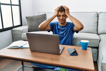 Poster - Young handsome hispanic man using laptop sitting on the floor suffering from headache desperate and stressed because pain and migraine. hands on head.