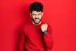 © Krakenimages.com - Young arab man with beard wearing casual red sweater angry and mad raising fist frustrated and furious while shouting with anger. rage and aggressive concept.