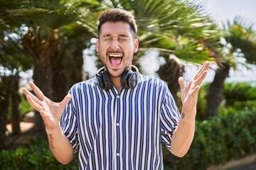 Sticker - Young handsome man listening to music using headphones outdoors celebrating mad and crazy for success with arms raised and closed eyes screaming excited. winner concept