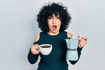 Poster - Young middle east woman holding italian coffee maker afraid and shocked with surprise and amazed expression, fear and excited face.