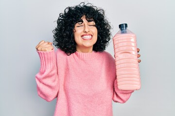 Sticker - Young middle east woman holding detergent bottle screaming proud, celebrating victory and success very excited with raised arm