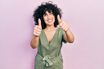 Sticker - Young middle east woman wearing casual clothes approving doing positive gesture with hand, thumbs up smiling and happy for success. winner gesture.