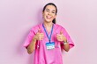 Young brunette woman wearing doctor uniform and stethoscope success sign doing positive gesture with hand, thumbs up smiling and happy. cheerful expression and winner gesture.