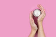 © Atlas - A jar of white cream in the hands of a woman on a pink background. Place for a logo. Face cream or skin care products.