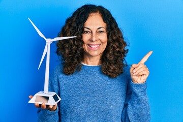 Sticker - Middle age hispanic woman holding solar windmill for renewable electricity smiling happy pointing with hand and finger to the side