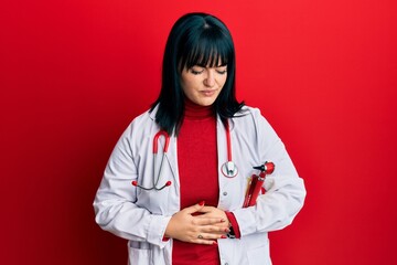 Sticker - Young hispanic woman wearing doctor uniform and stethoscope with hand on stomach because indigestion, painful illness feeling unwell. ache concept.