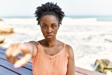 Canvas Print - Young african american woman wearing summer clothes standing at the beach pointing with finger to the camera and to you, confident gesture looking serious