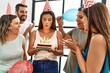 © Krakenimages.com - Young hispanic woman smiling happy and holding birthday cake standing with a group of friends at home.