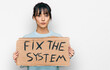 © Krakenimages.com - Young hispanic woman holding fix the system banner cardboard thinking attitude and sober expression looking self confident