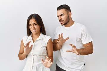 Poster - Young interracial couple standing together in love over isolated background disgusted expression, displeased and fearful doing disgust face because aversion reaction. with hands raised