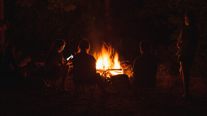 Tourism and rest. Silhouettes of people in the dark on the background of a campfire with sparks. Communication and friendship.