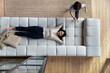 © fizkes - Above top view relaxed peaceful happy young korean woman lying resting on comfortable couch while energetic active little child boy running around, having fun in living room, daycare concept.