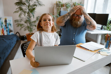 Wall Mural - Surprised little girl does homework on laptop while father clutches head at home