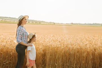 Side view of a family of farmers woman mother and kid daughter both with hats on their heads near a large field of golden wheat. harvesting time