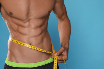 Wall Mural - Shirtless man with slim body and measuring tape around his waist on light blue background, closeup