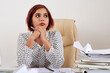 © DragonImages - Portrait of pretty pensive female entrepreneur sitting at office desk with stacks of documents and reports