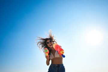 Canvas Print - African American woman with water guns against blue sky, low angle view