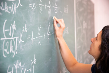 Wall Mural - Female student or teacher in the classroom writing on chalkboard mathematical equations