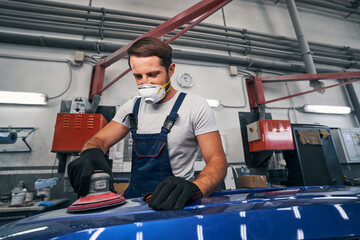 Poster - Man in car repair shop sanding automobile with tool