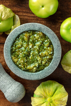 Tomatillos, green tomatoes, with salsa verde, green sauce, in a molcajete, traditional Mexican mortar, top shot on a dark rustic wooden background
