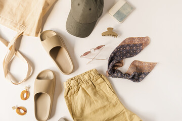 Wall Mural - Neutral dusty beige color women fashion clothes and accessories for summer vacation beach chill. Cap, slippers, sunglasses, barrette, shorts, shopper bag on white background. Flat lay, top view