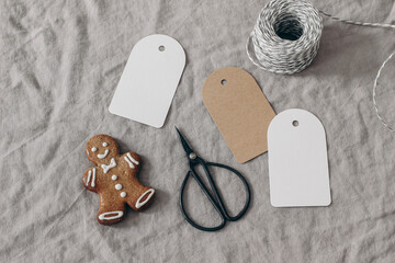 Wall Mural - Christmas still life. Blank paper gift tags, labels mockups. Gingerbread cookie, black vintage scissors and decorative rope on beige linen tablecloth. Gift wrapping concept. Winter sale. Flat lay, top