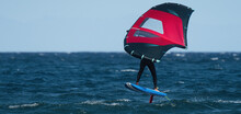 A Man Is Wing Foiling Using Handheld Inflatable Wings And Hydrofoil Surfboards In A Blue Ocean, Rider On A Wind Wing Board, Surf The Waves