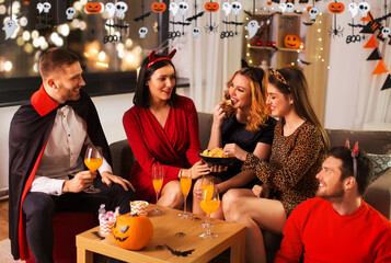 Poster - friendship, holiday and people concept - group of happy smiling friends in halloween costumes of vampire, devil, witch and cheetah at home party at night