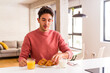 © Asier - Young mixed race man eating croissant in a kitchen on the morning