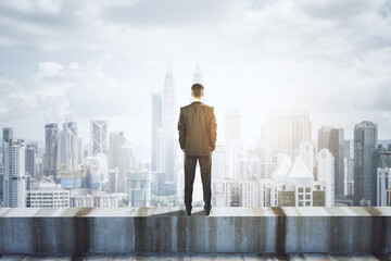 Wall Mural - back view of young businessman standing on concrete edge of building on city background with mock up