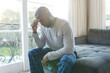© WavebreakMediaMicro - Worried, sad african american man thinking, sitting on couch holding head in living room