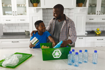 Wall Mural - Happy african american father and son in kitchen talking and sorting rubbish for recycling