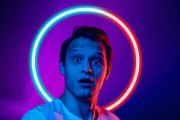 Young man's portrait isolated on blue studio background in multicolored neon light with geometric luminescent shape cirlce