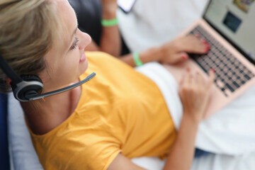 Woman in headphones with microphone lies on bed and works on laptop