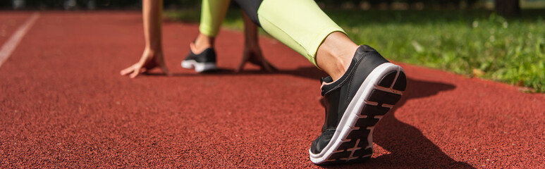 cropped view of sportswoman in starting pose on stadium, banner