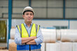 © Supachai - Asian male engineer wearing safety vest and hardhat standing with arms crossed in warehouse factory Industrial