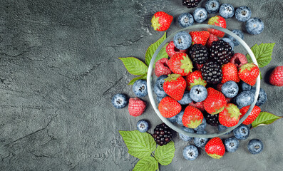 Wall Mural - berries of raspberries, strawberries, blackberries and blueberries in a plate on a concrete table, top view