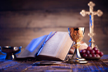 Catholic religion concept. Catholic symbols composition. The Cross, Holy Bible, rosary and golden chalice on the altar.