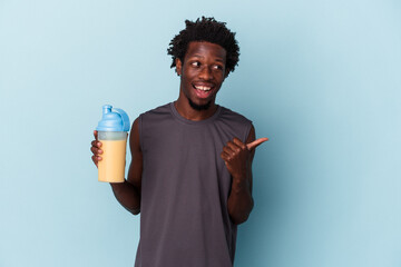 Young african american man holding protein milkshake isolated on blue background points with thumb finger away, laughing and carefree.