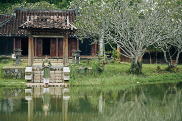 Poster - Young woman in traditional dress holding wooden fan when standing on steps of temple next to beautiful pond